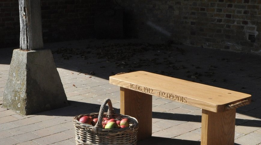A small oak bench carved with dates, beside a basket of apples